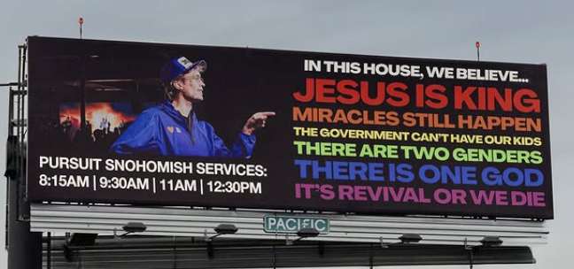 A large billboard displaying a message about beliefs including 'Jesus is King' and 'There is one God', with a man gesturing while wearing a blue jacket and hat. Below, it lists service times for 'Pursuit Snohomish'.